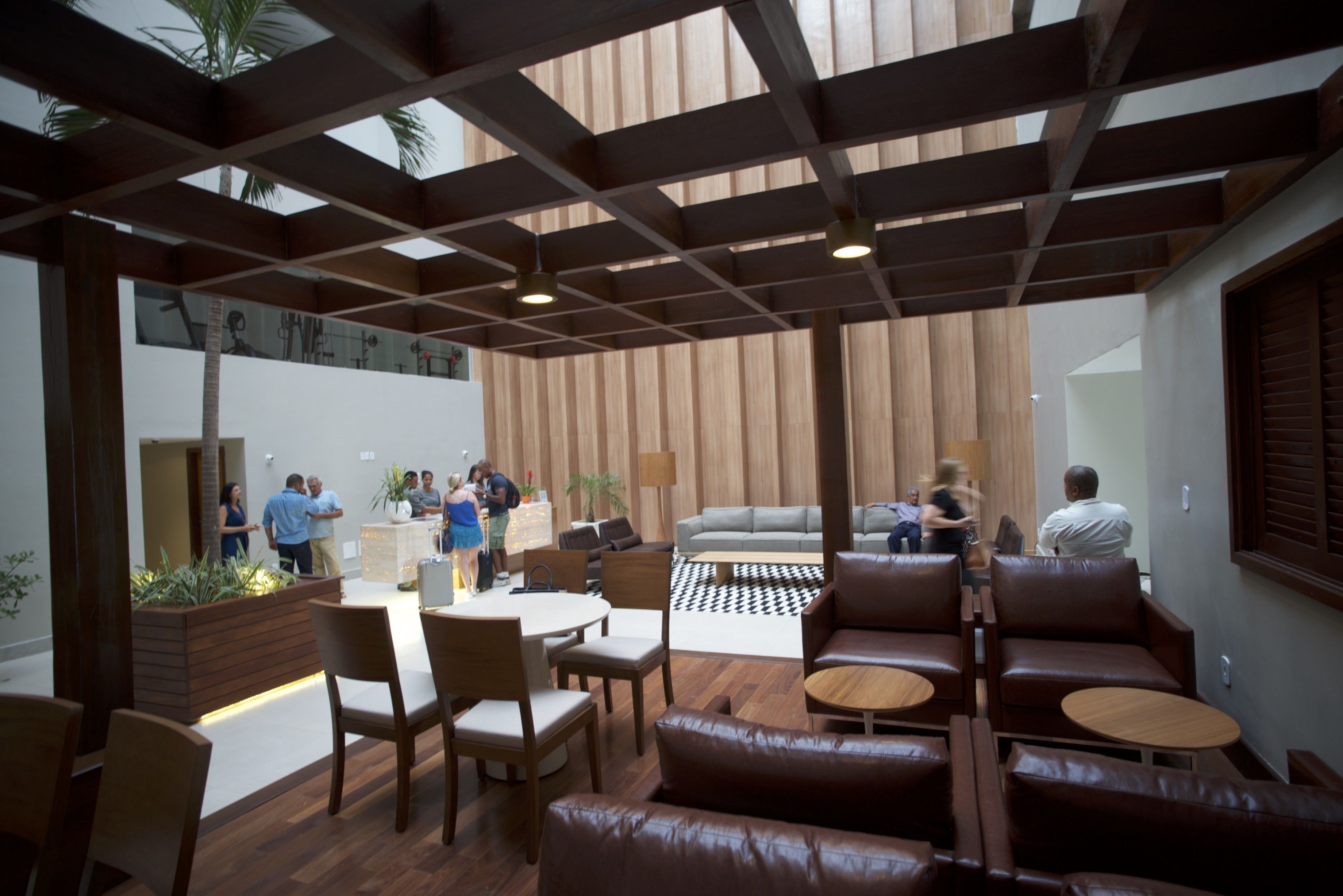 A modern indoor space with wooden flooring, a central seating area with leather couches and round tables, and a high ceiling with exposed beams.