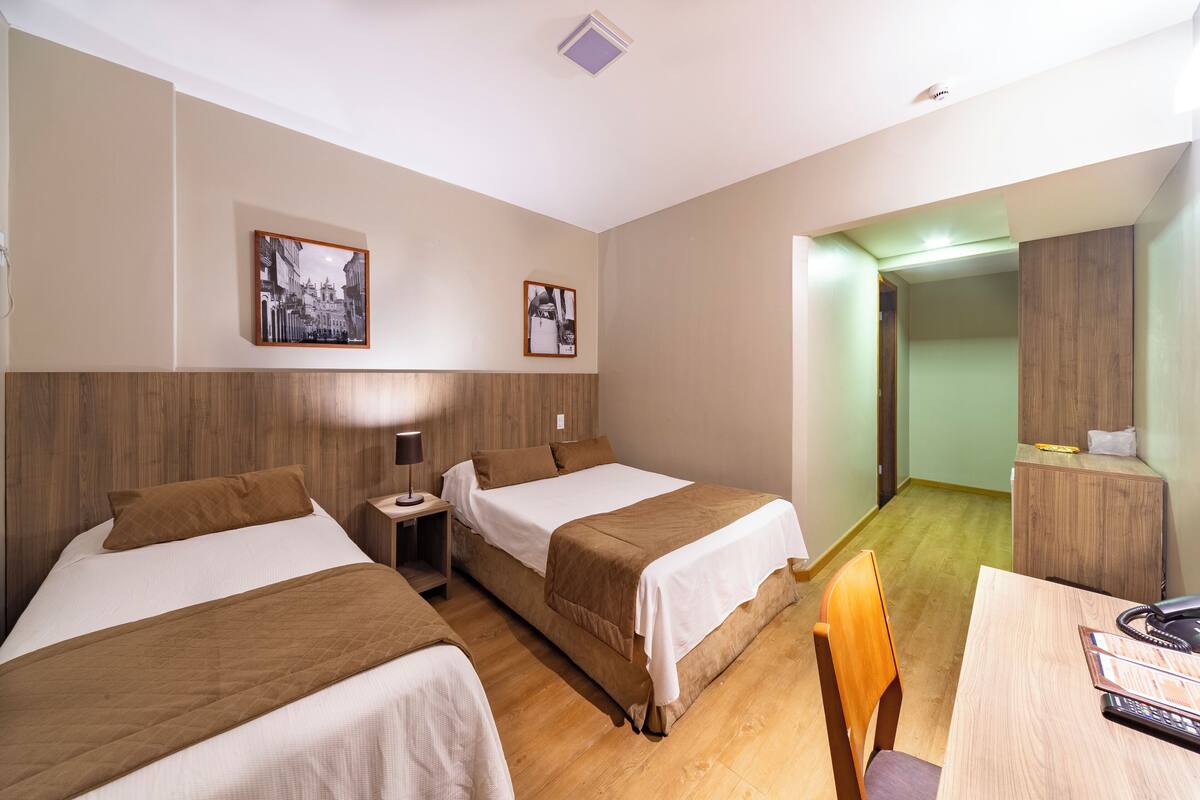 A hotel room with two beds, a desk, and a chair. There are two framed pictures on the wall.