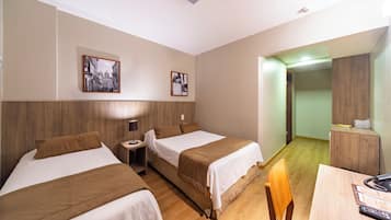 Quarto de hotel com duas camas, uma escrivaninha e uma cadeira. Há duas molduras com quadros na parede.