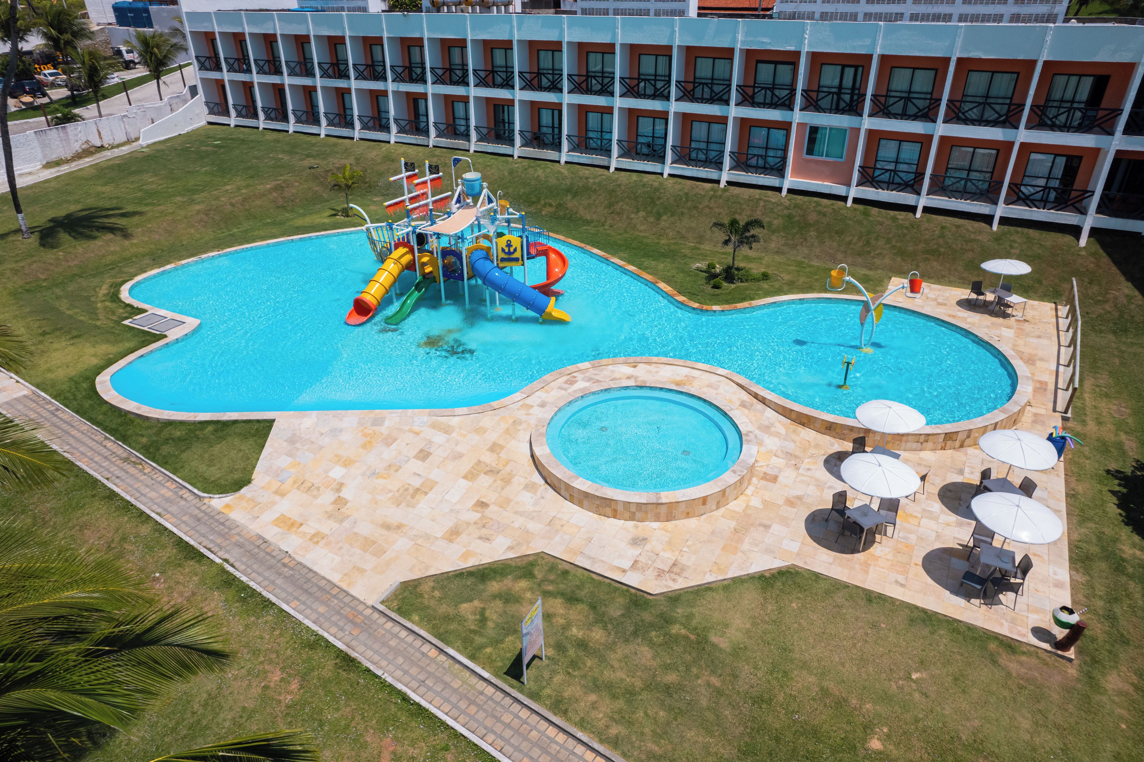 Una piscina con tobogán de agua y una zona circular separada con tumbonas y sombrillas.