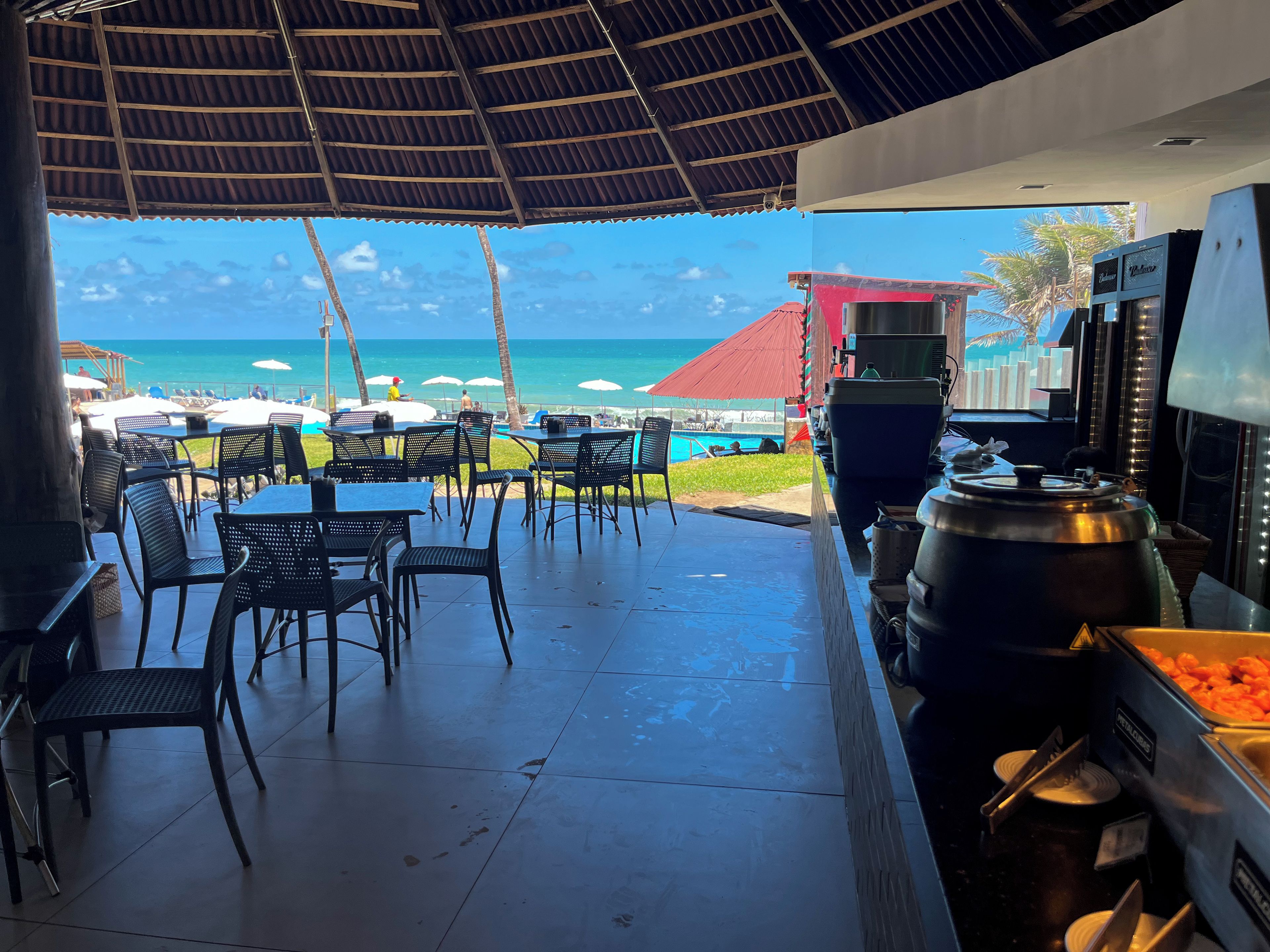 Un espace extérieur aménagé avec des tables et des chaises, une vue sur l’océan et un bar doté d’une grande cuve à bière.