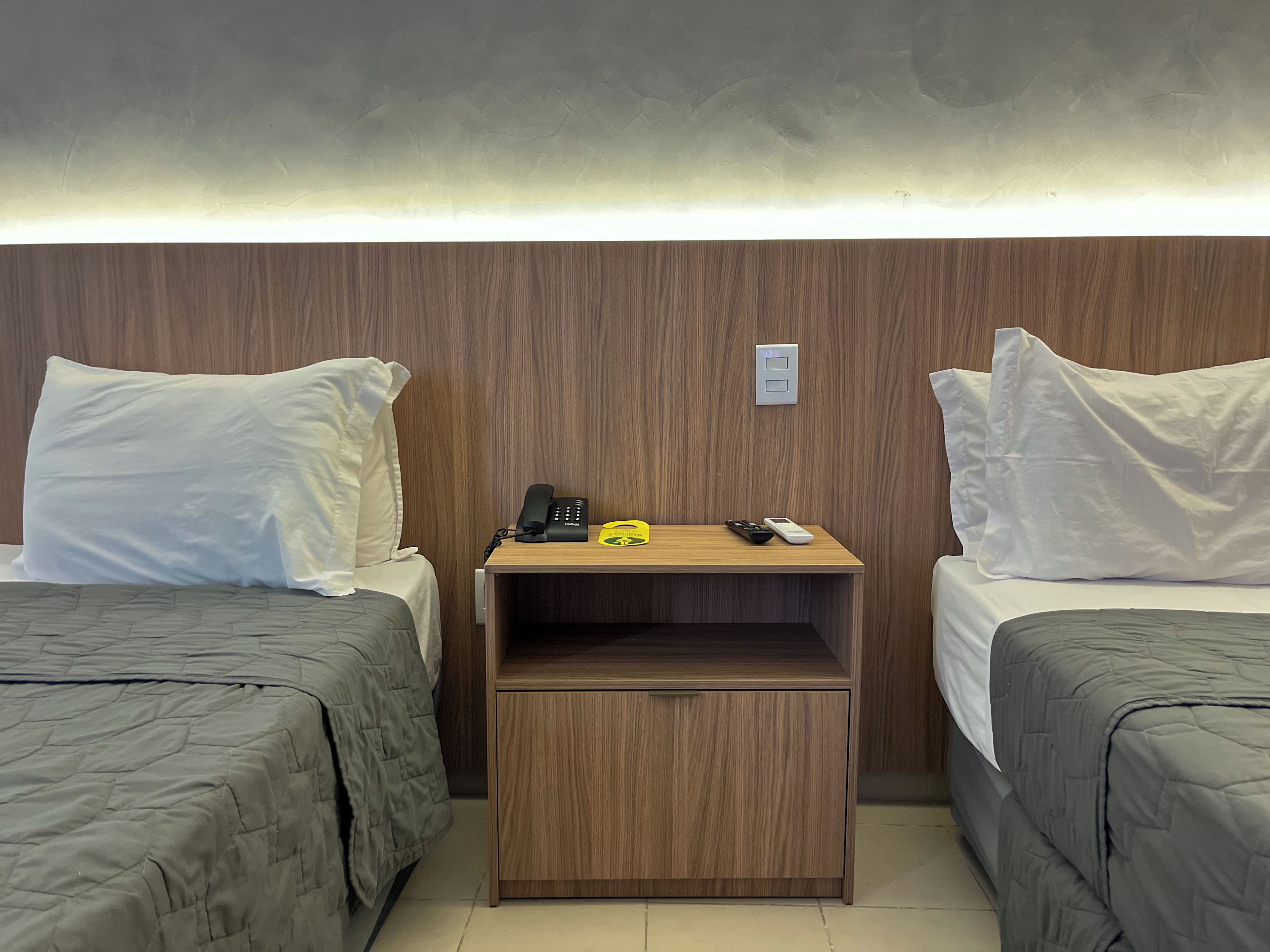 Habitación de hotel con dos camas, una mesita de noche de madera con un teléfono, controles remotos y un pequeño armario.