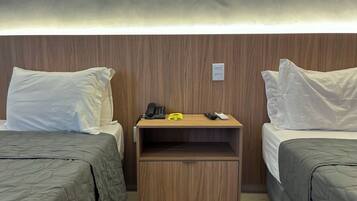 Habitación de hotel con dos camas, una mesita de noche de madera con un teléfono, controles remotos y un pequeño armario.