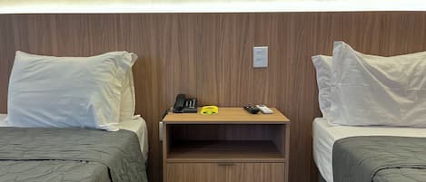 A hotel room with two beds, a wooden nightstand with a phone, remote controls, and a small cabinet.