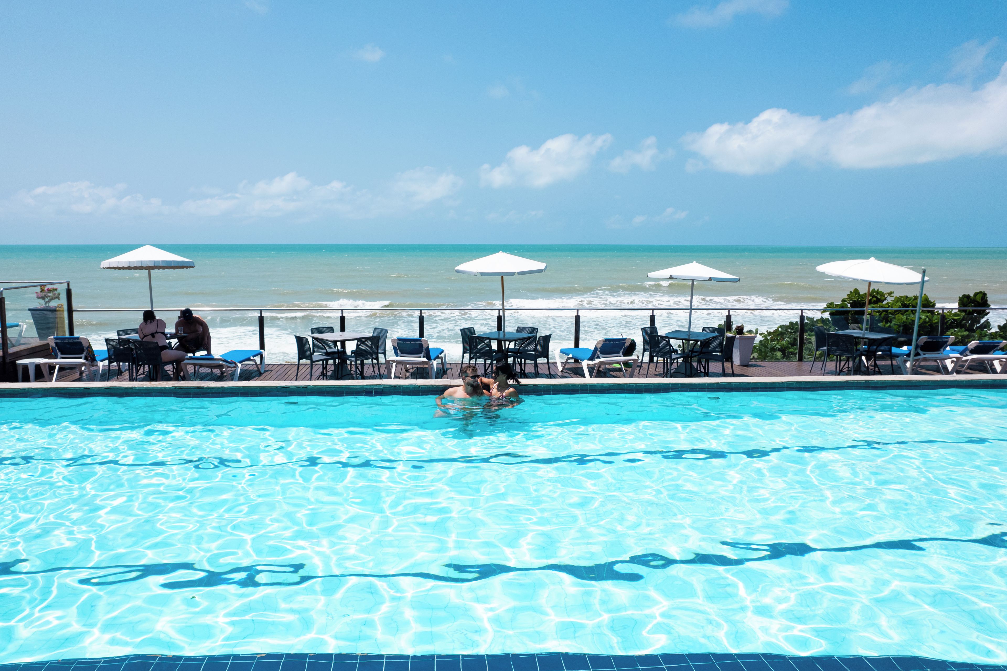 Una piscina con agua cristalina azul, rodeada de sillones de descanso y sombrillas, con vista al océano.