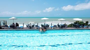 Una piscina con agua cristalina azul, rodeada de sillones de descanso y sombrillas, con vista al océano.