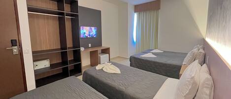 A hotel room with two beds, a TV on the wall, a wardrobe, and a window with curtains.