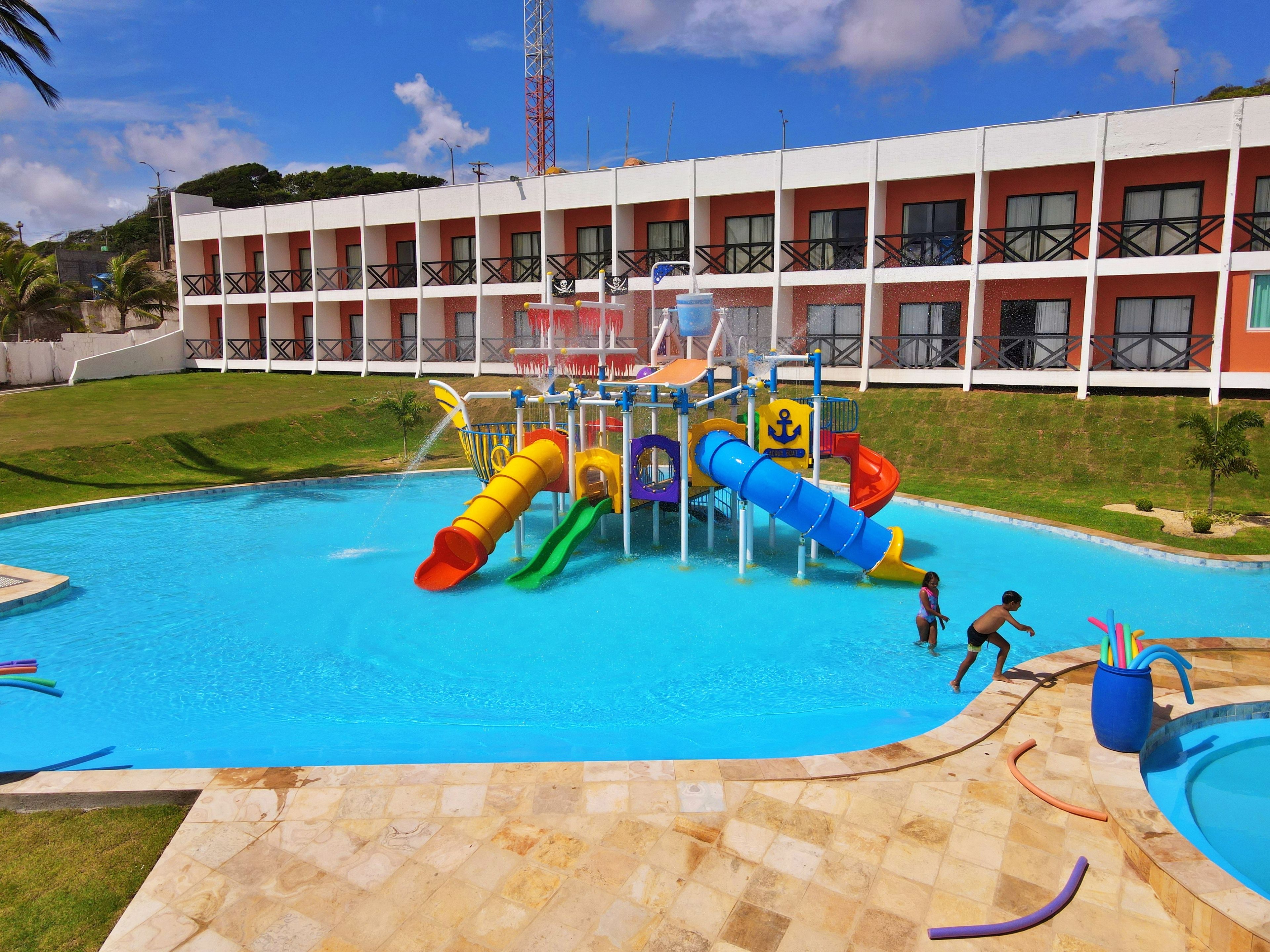 Une piscine avec un toboggan et un bâtiment doté de balcons en arrière-plan.