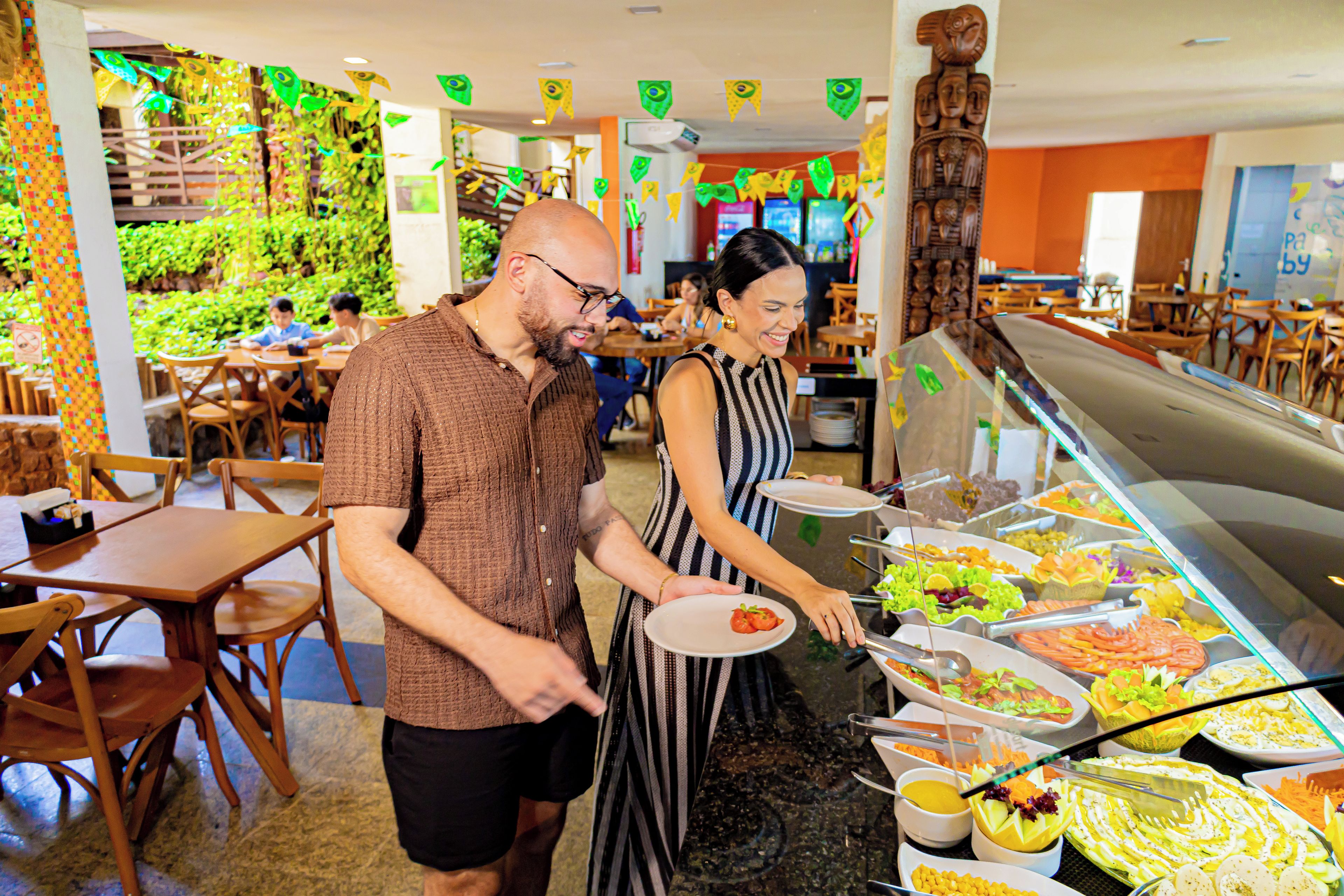 Espaço de buffet com diversas opções de comida e área de estar com mesas e cadeiras.