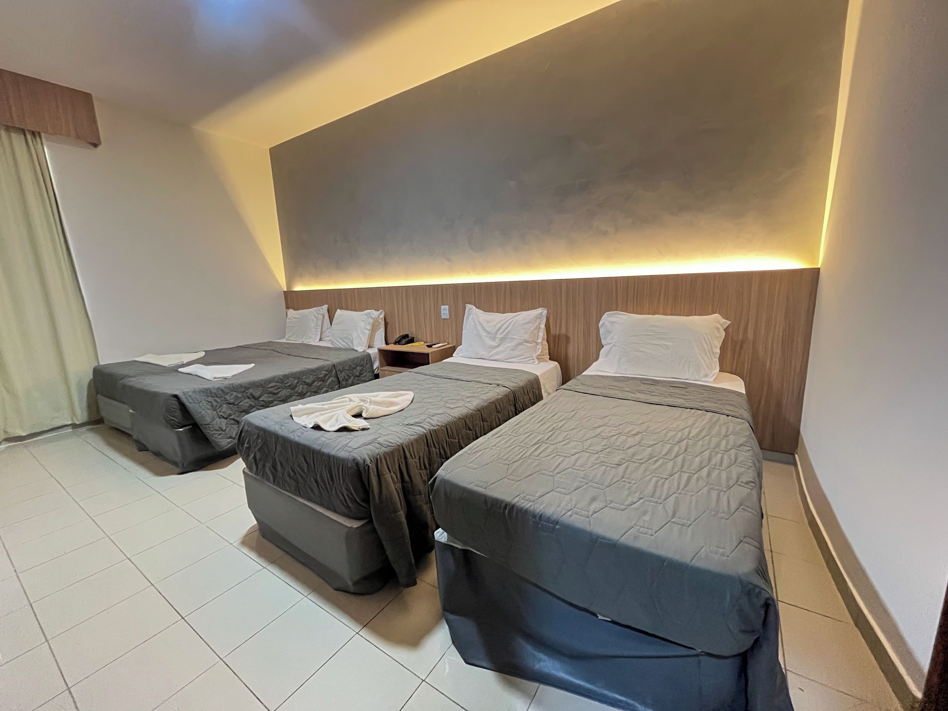 A hotel room with two single beds, a nightstand, and a large wall-mounted light.
