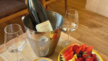 Una botella de vino en un balde, dos copas, un plato con fruta y tiramisú, y dos copas vacías sobre una mesa de madera.