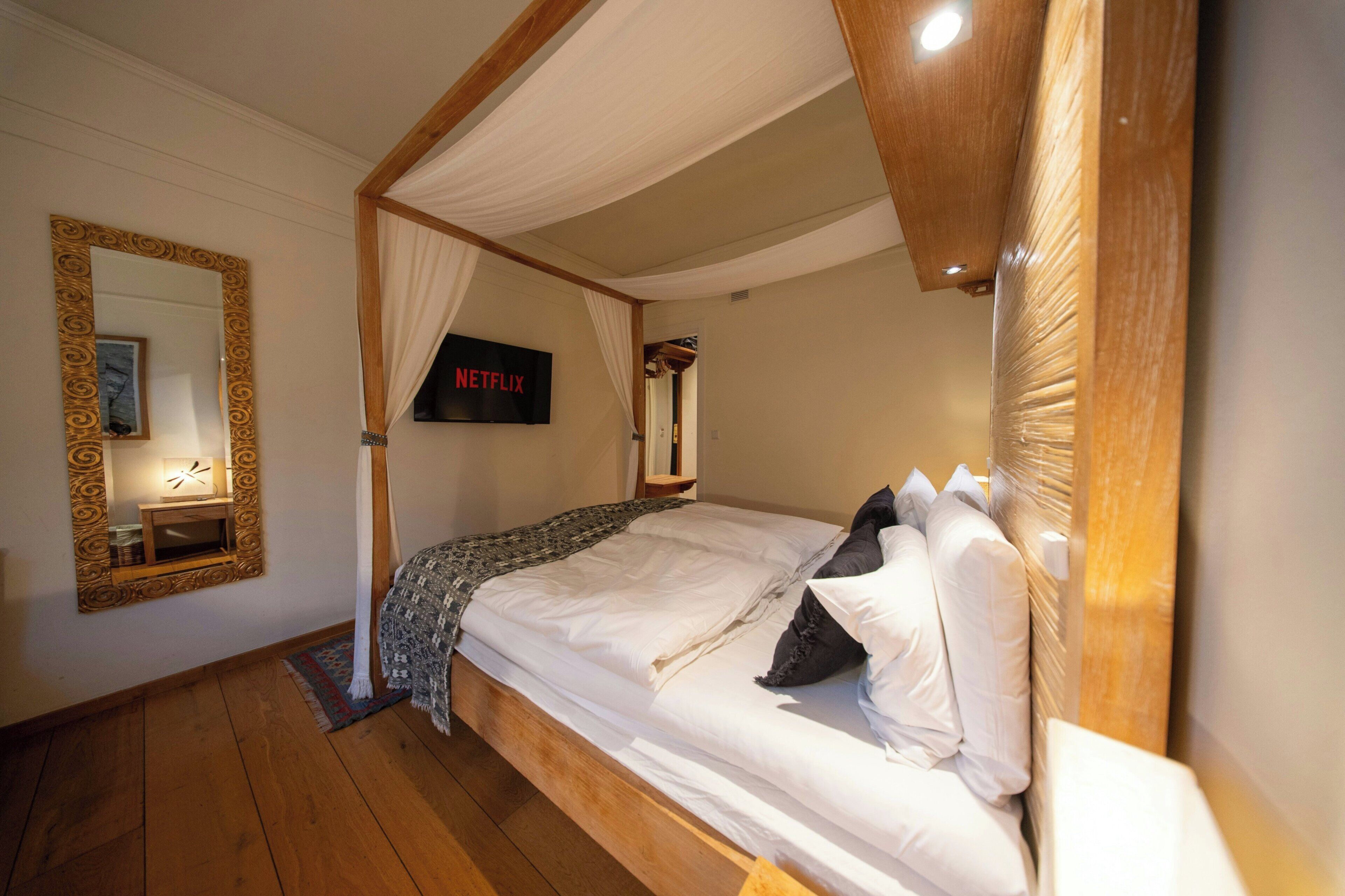 Un dormitorio con cama con dosel, televisor montado en la pared y espejo con marco decorativo.