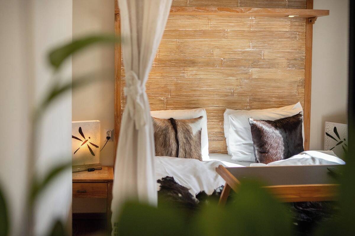 A bed with white linens, a wooden headboard, and two pillows. There is a bedside table with a lamp.