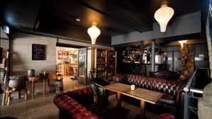 Un espace salon confortable avec des fauteuils en cuir, une table en bois et un bar en arrière-plan.