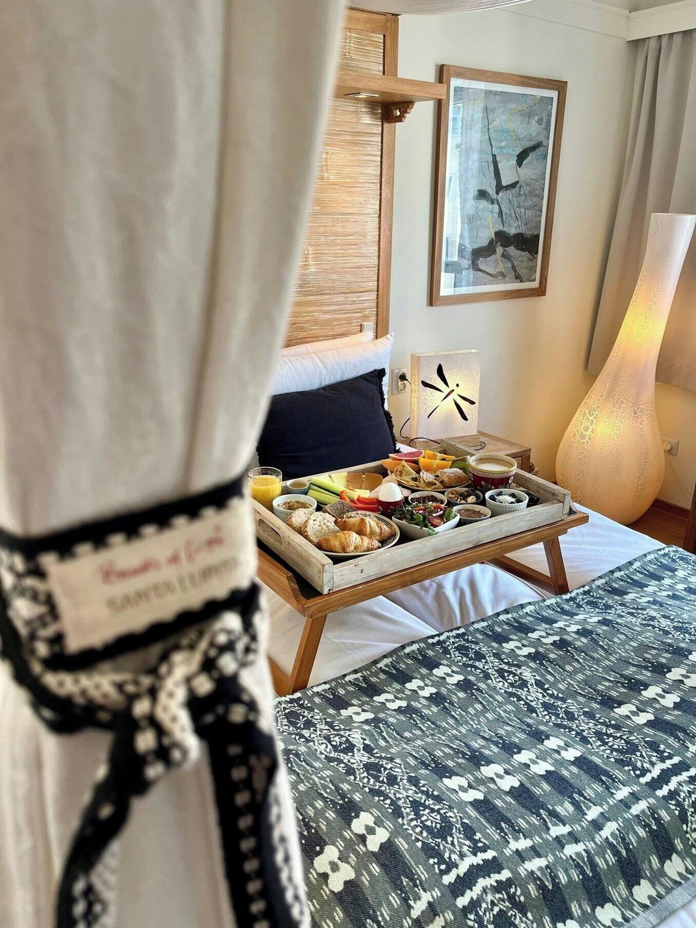 Una habitación de hotel con un carrito de desayuno en la cama, una lámpara y un cuadro en la pared.