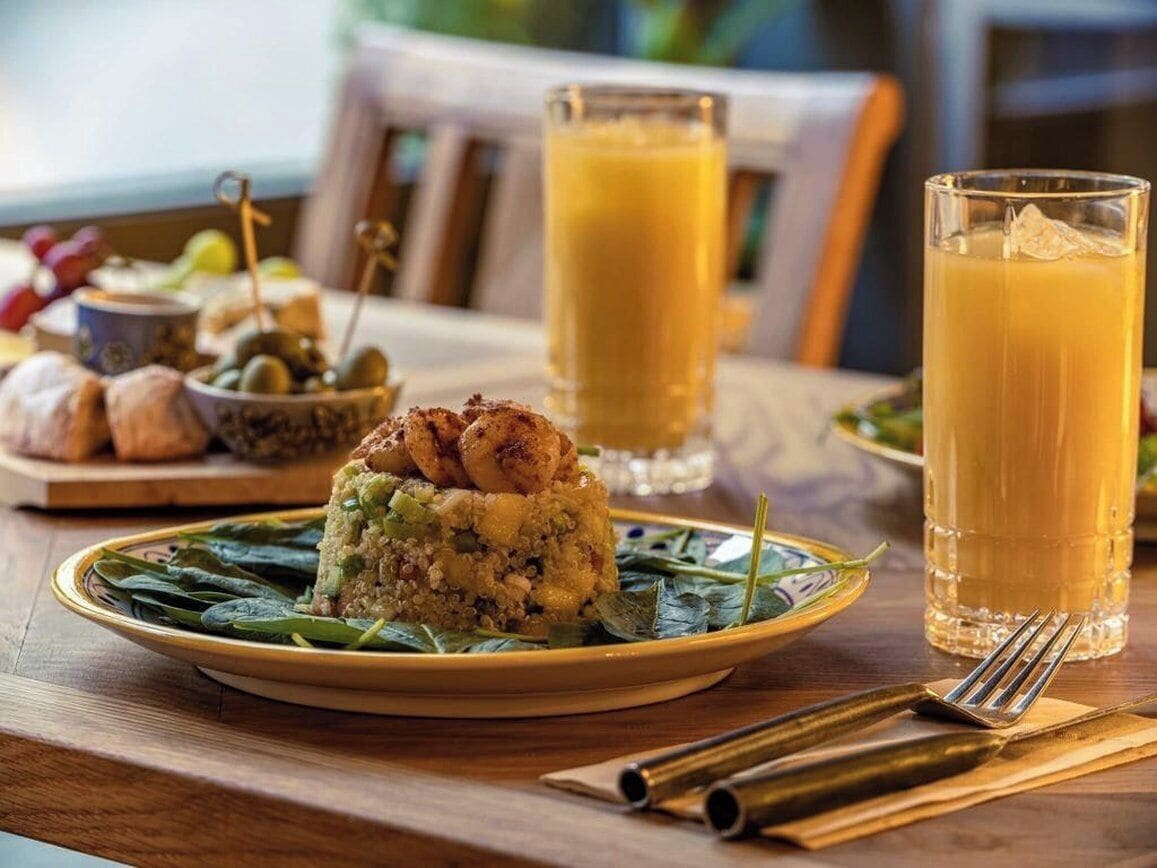 A breakfast setting with a plate of food, two glasses of orange juice, and a bowl of olives.