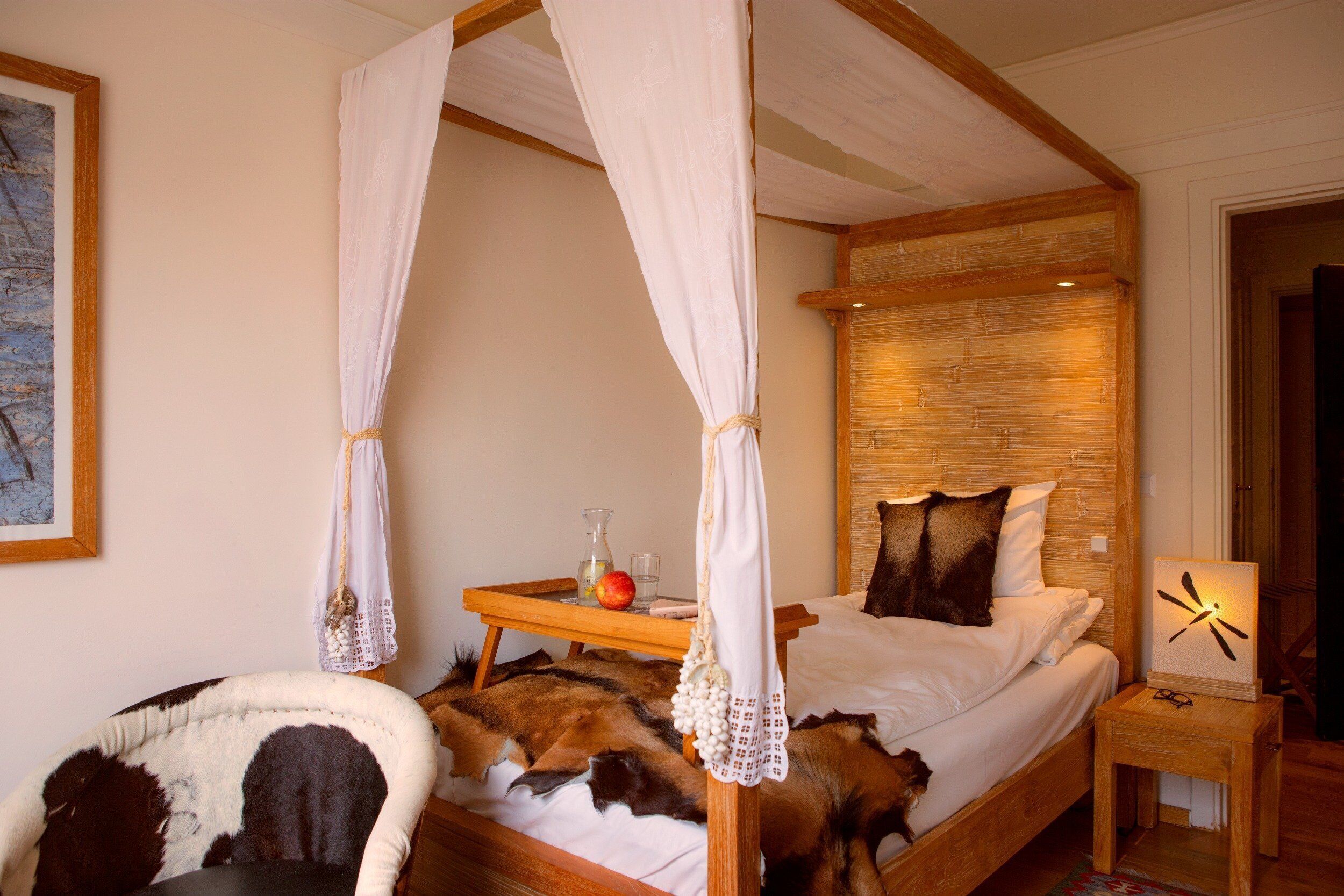 Een hemelbed met baldakijn, een nachtkastje met een klok en een houten hoofdeinde.
