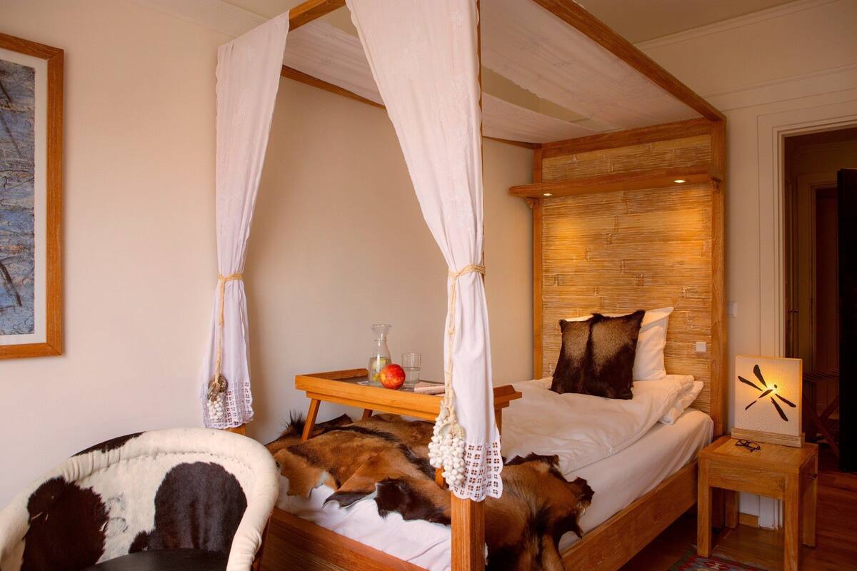 A four-poster bed with a canopy, a bedside table with a clock, and a wooden headboard.