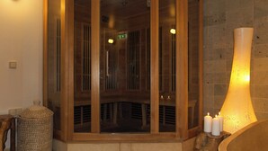 Un sauna en bois avec une porte en verre, un mur de pierres et trois bougies allumées posées sur une étagère en pierre.