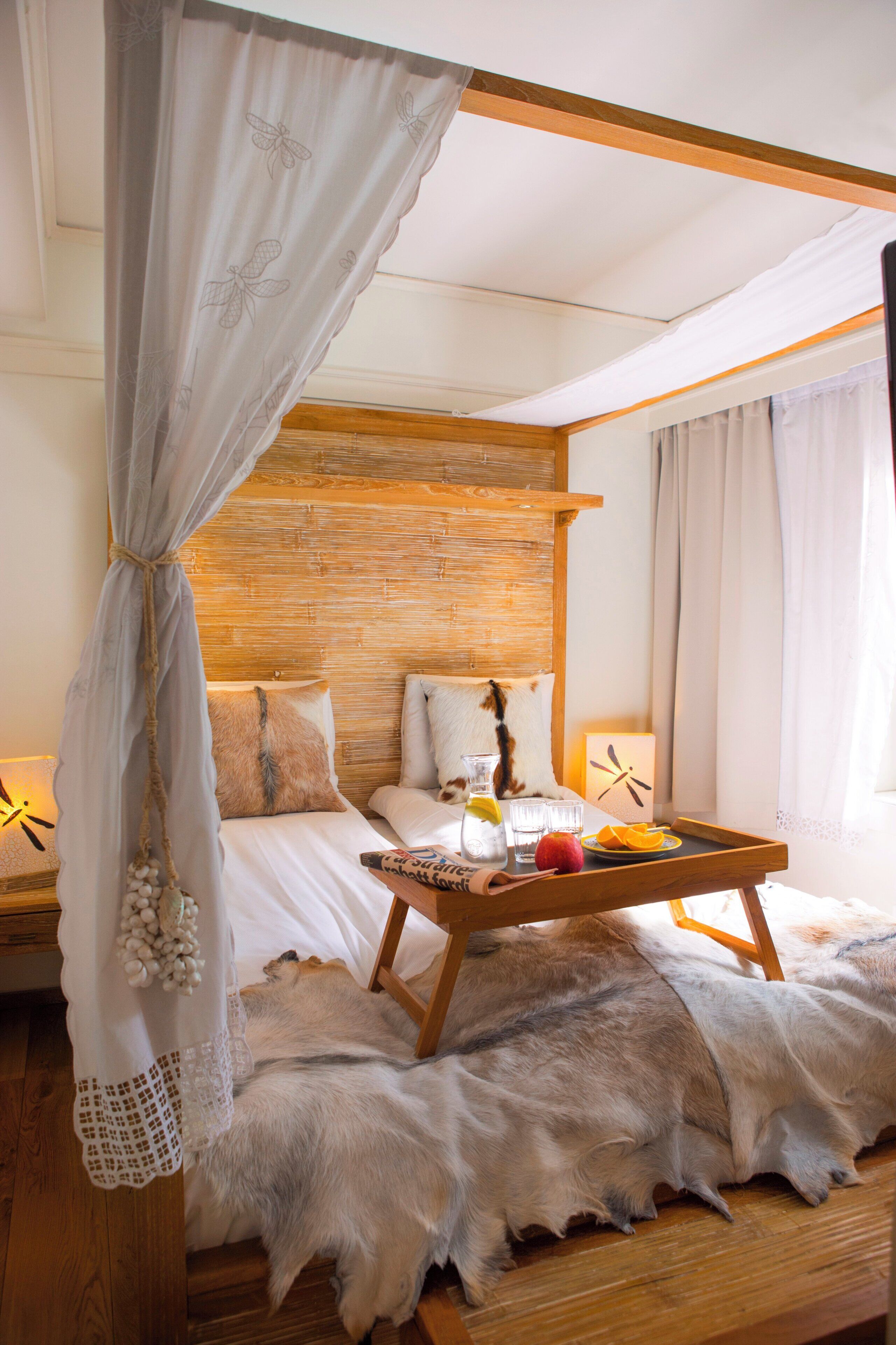 A bedroom with a wooden headboard, a bed with white linens, a wooden nightstand, a glass of water, a fruit bowl, and a decorative item on the nightstand.