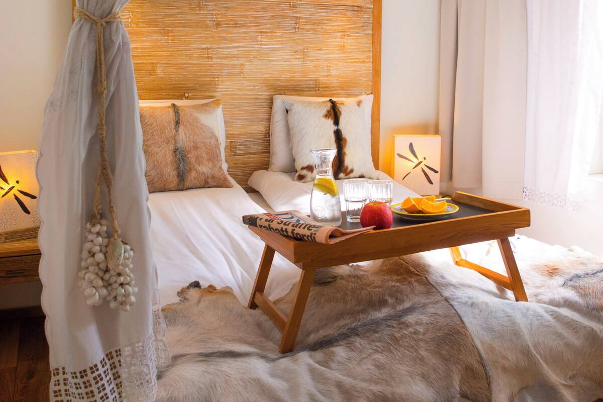 A bedroom with a wooden headboard, a bed with white linens, a wooden nightstand, a glass of water, a fruit bowl, and a decorative item on the nightstand.