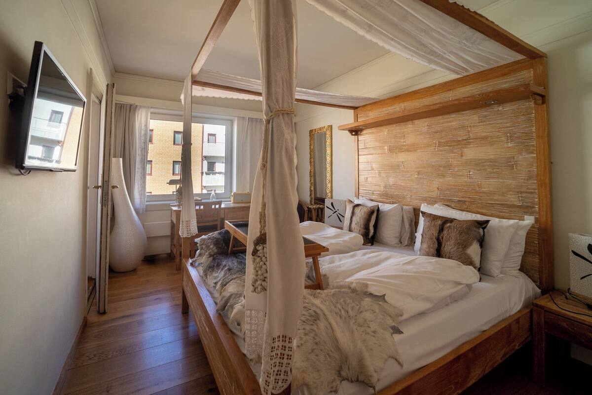 A bedroom with a four-poster bed, a large mirror, and a view of the outside balcony.