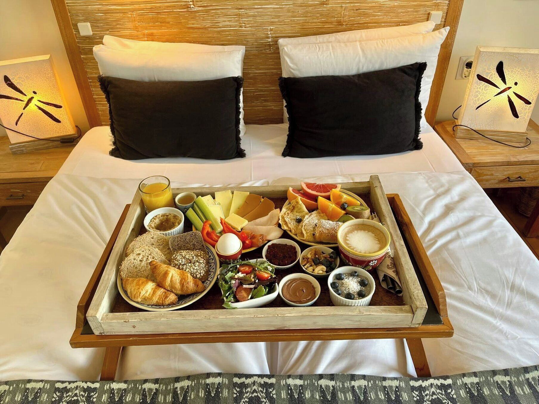 Una cama con una bandeja de desayuno que incluye pan, frutas y bebidas.