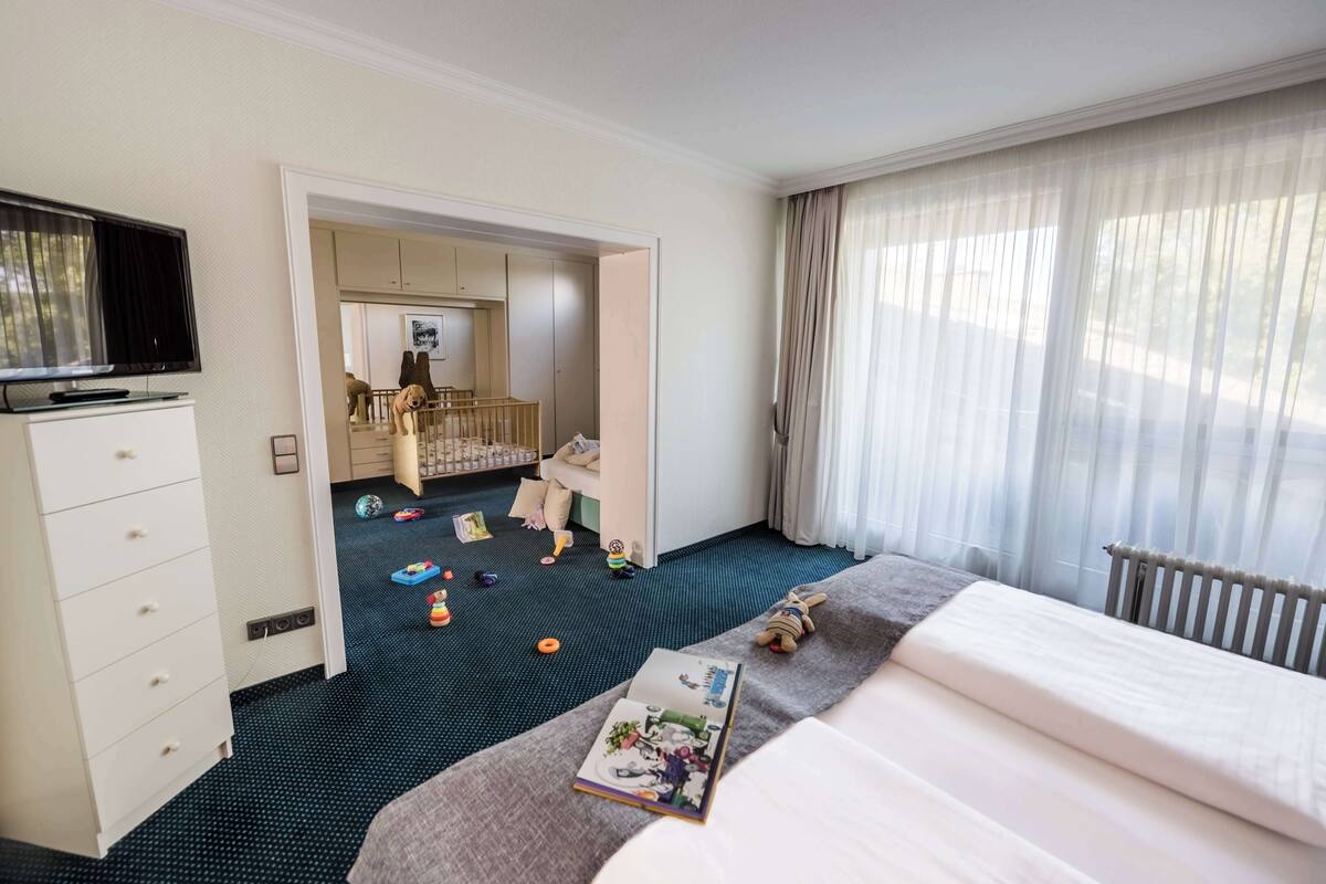 Een hotelkamer met een bed, een televisie, een kledingkast en een speelhoek met speelgoed.