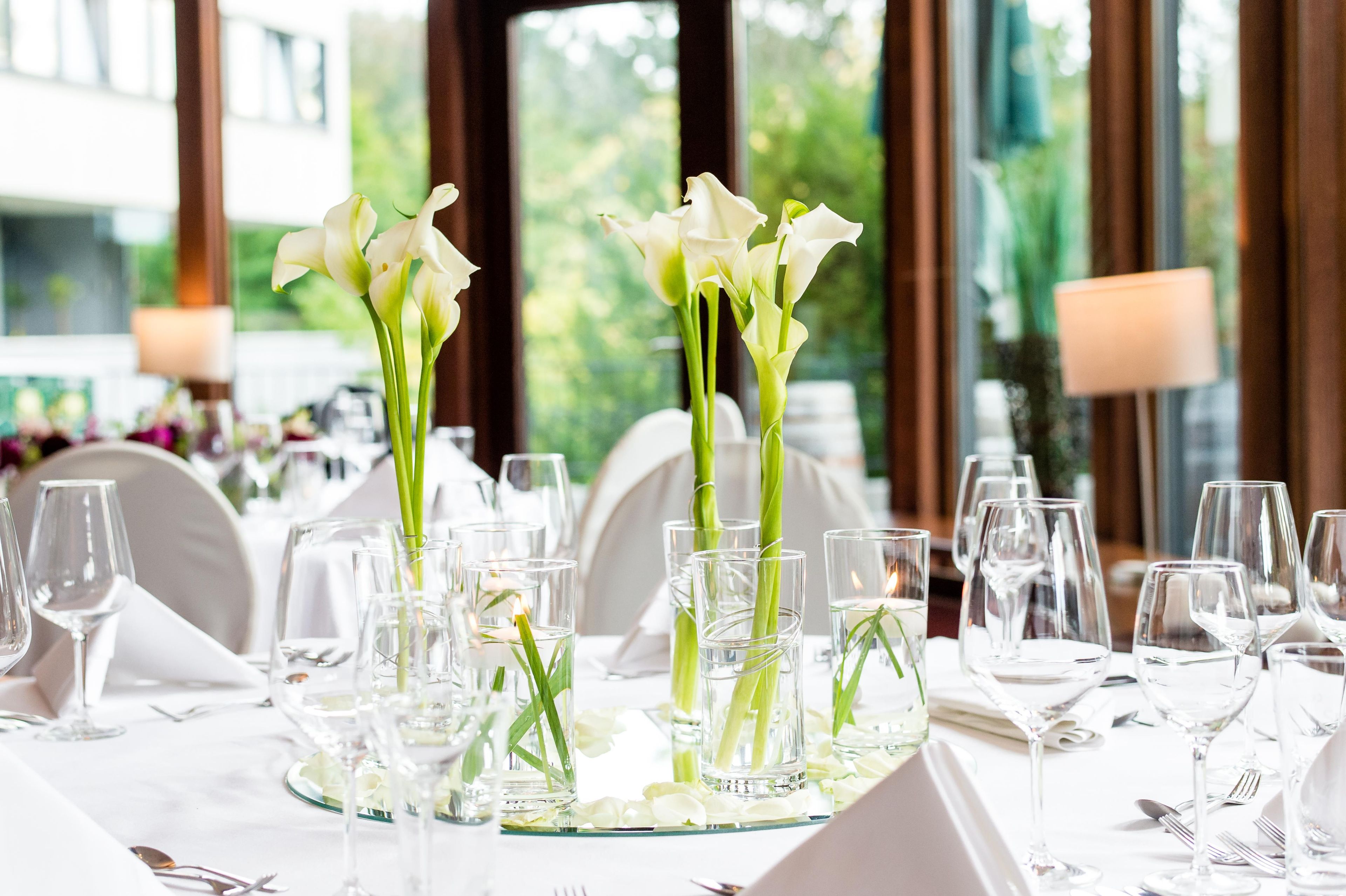 Tavola imbandita per un evento formale, con bicchieri trasparenti e fiori bianchi.