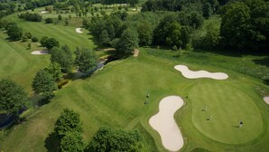 An aerial view of a golf course with sand bunkers, trees, and a small water body.