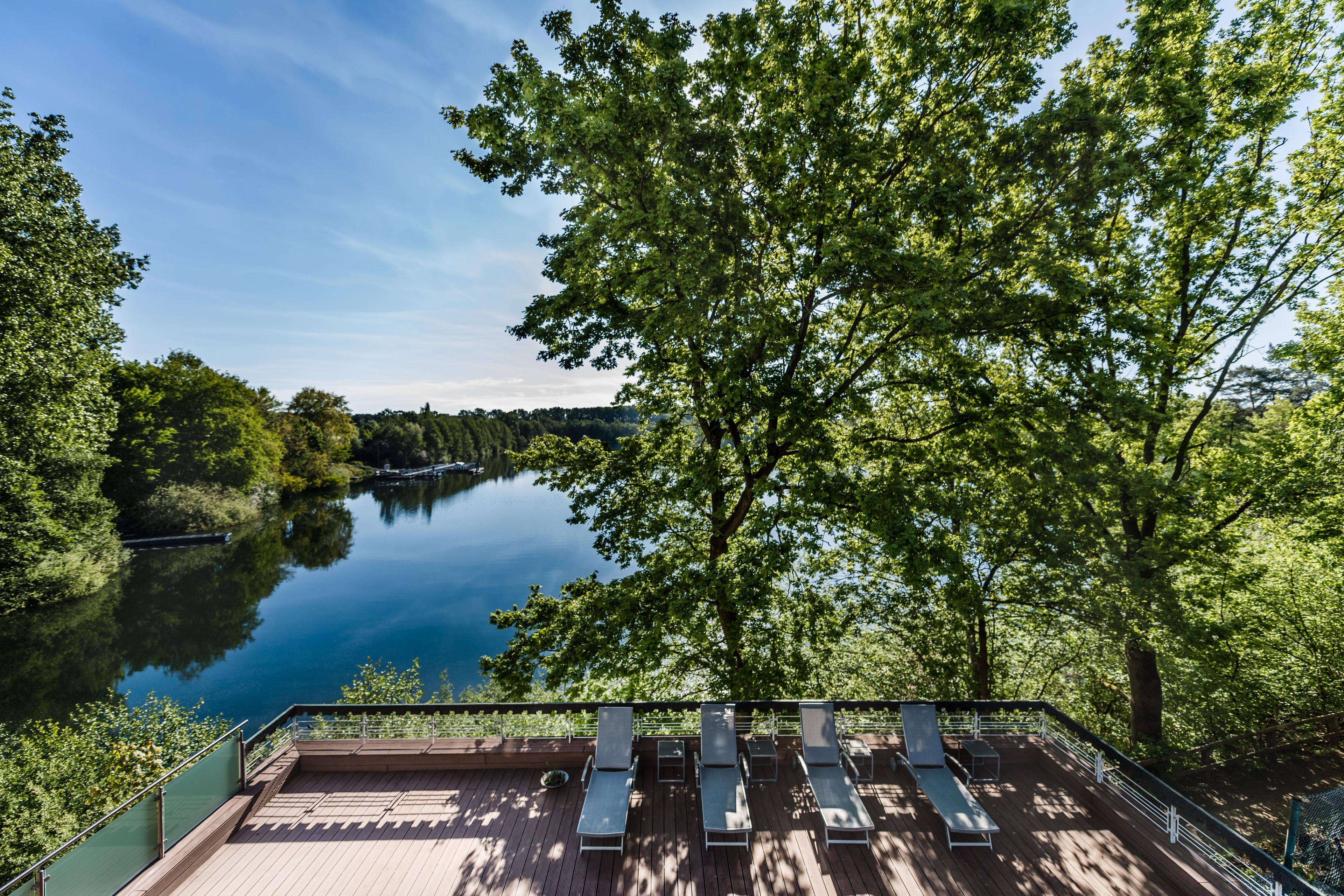 Eine Terrasse mit Liegestühlen mit Blick auf einen stillen See, der von Bäumen umgeben ist.