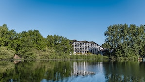 Un hotel de varios pisos, ubicado junto a un lago tranquilo, rodeado de abundante vegetación.