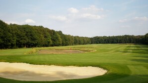A golf course with sand bunkers, a putting green, and a forested area in the background.