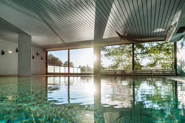 An indoor swimming pool with clear water, large windows, and a wooden ceiling.