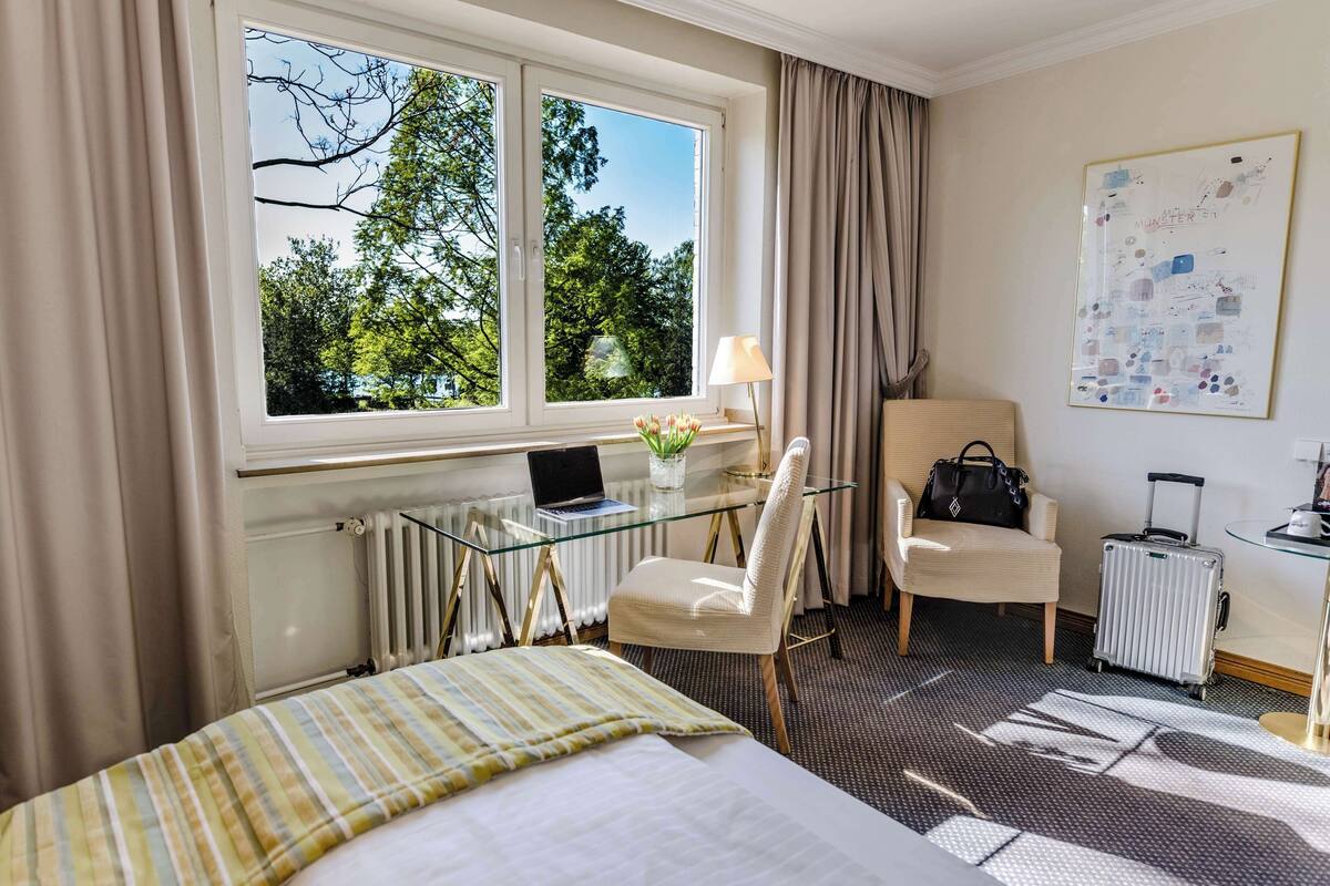 Hotelkamer met een bed, bureau met een laptop, stoel, koffer en een radiator.