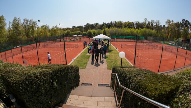 A tennis court with a net, surrounded by a fence and trees.