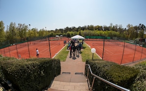 A tennis court with a net, surrounded by a fence and trees.