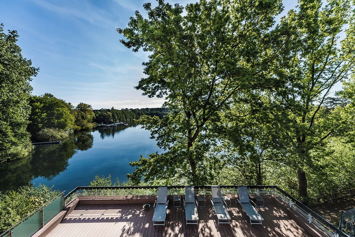 A deck with lounge chairs overlooking a calm lake, surrounded by lush greenery.