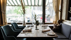 Een restaurant met een houten tafel gedekt voor een maaltijd, een vaas met groen en uitzicht op de straat.