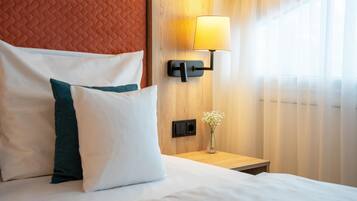 Ein ordentlich bezogenes Bett mit weißen und türkisfarbenen Kissen, einer Nachttischlampe und einem kleinen Blumenvasen auf einem Holznachttisch.