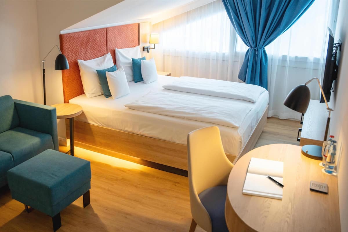 Een moderne hotelkamer met een bed, een bank, een stoel, een bureau en een lamp.