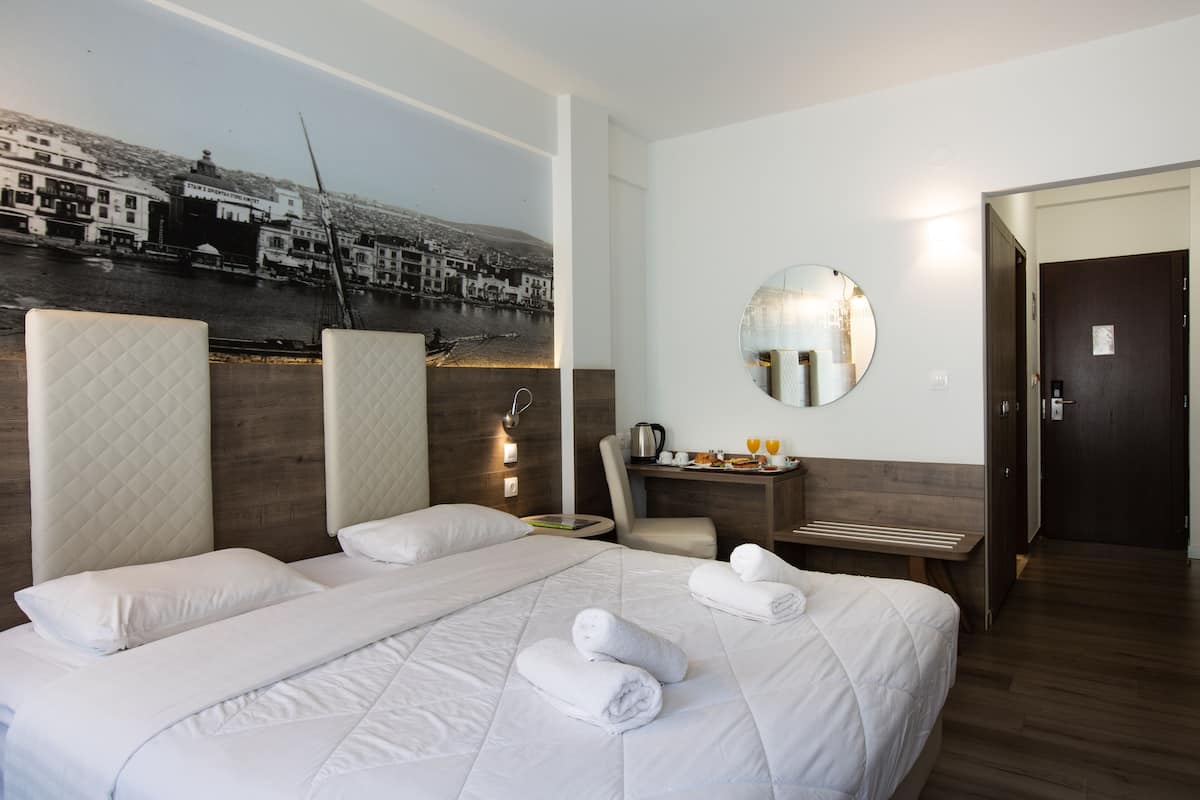 A hotel room with a large bed, a desk with a mirror, and a view of a coastal town.