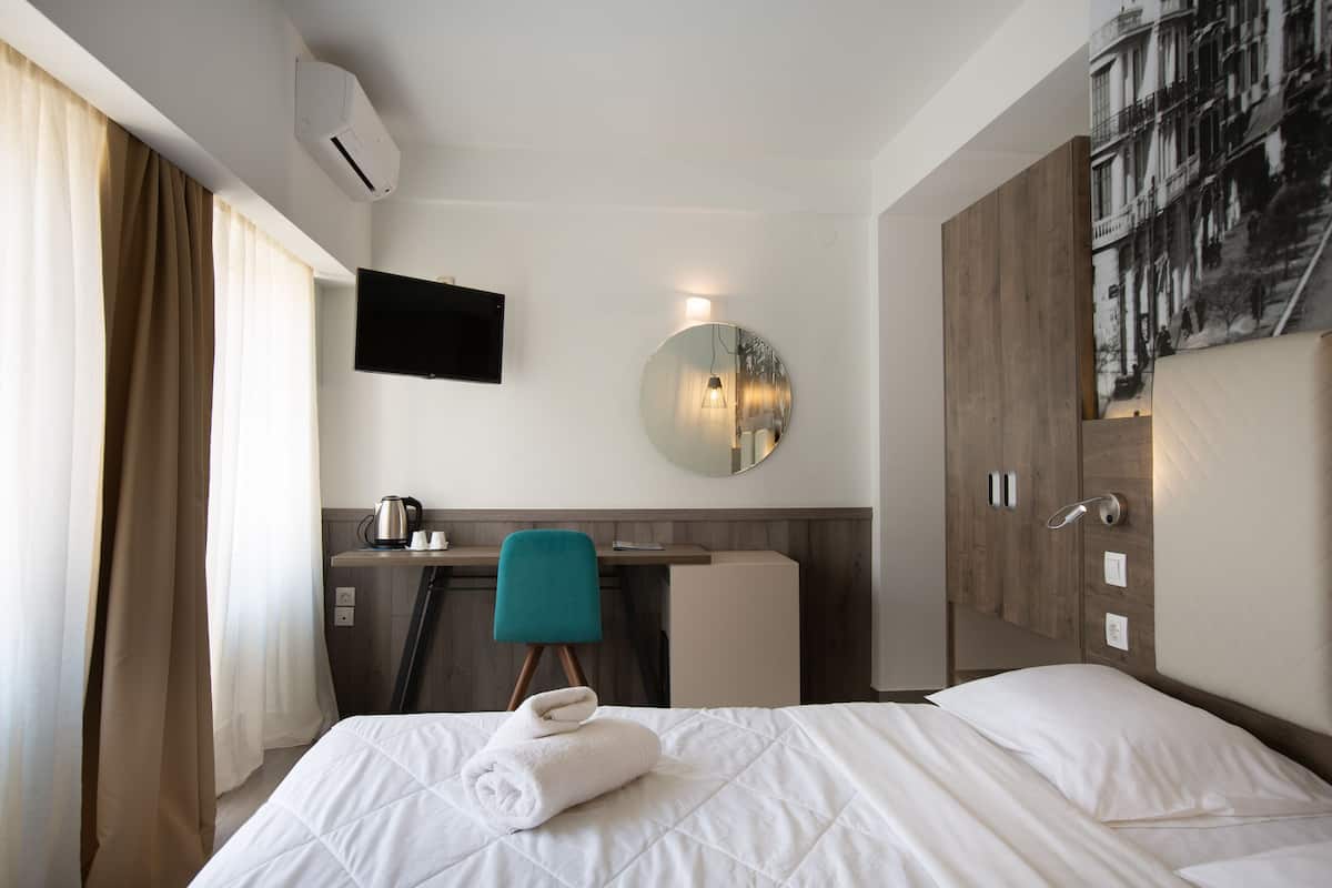 A hotel room with a bed, a desk, a chair, a flat-screen TV, a round mirror, and a wardrobe.