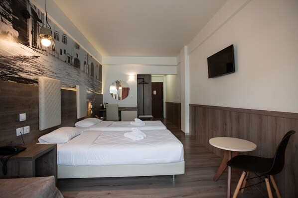 A hotel room with a large bed, a bedside table with a phone, a small round table with a chair, and a flat-screen TV mounted on the wall. - Metropolitan Hotel (Thessaloniki)