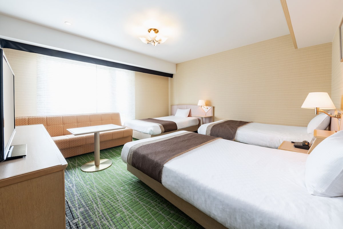 Ein Hotelzimmer mit zwei Einzelbetten, einer Schlafcouch, einem Schreibtisch und einem kleinen Tisch.