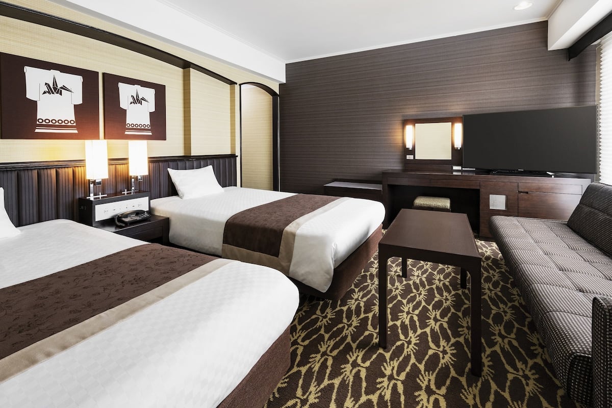 Ein Hotelzimmer mit zwei Betten, einem Fernseher, einem Schreibtisch und einer Couch.