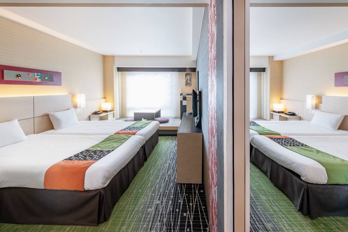 Ein Hotelzimmer mit zwei Betten, einem Fernseher, einem Schreibtisch und einem Fenster.