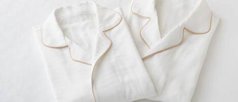 Two neatly folded white pillows with gold piping on a white textured surface.