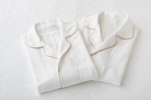 Two neatly folded white pillows with gold piping on a white textured surface.