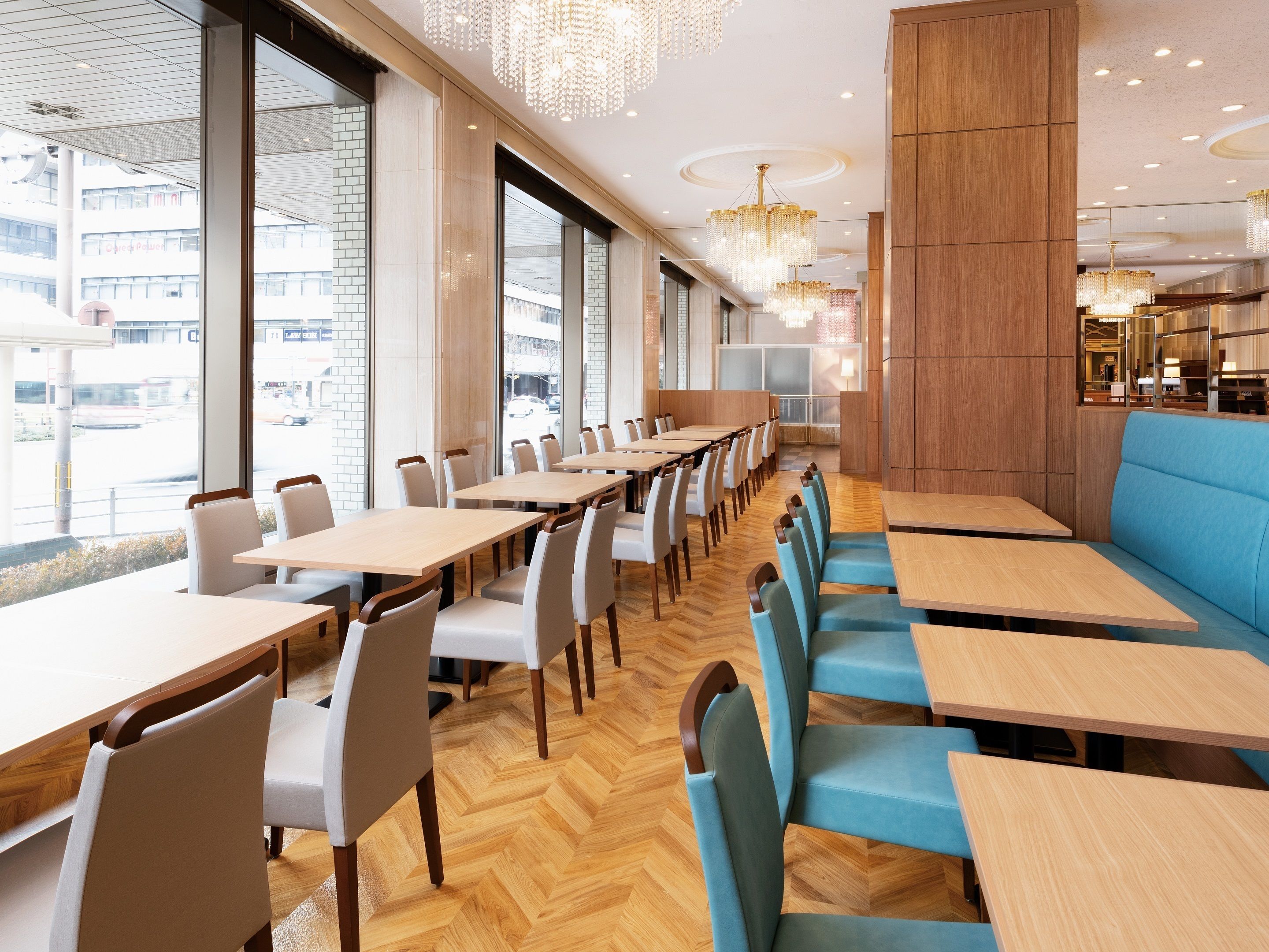 A modern restaurant with long tables and chairs, large windows, and decorative chandeliers.